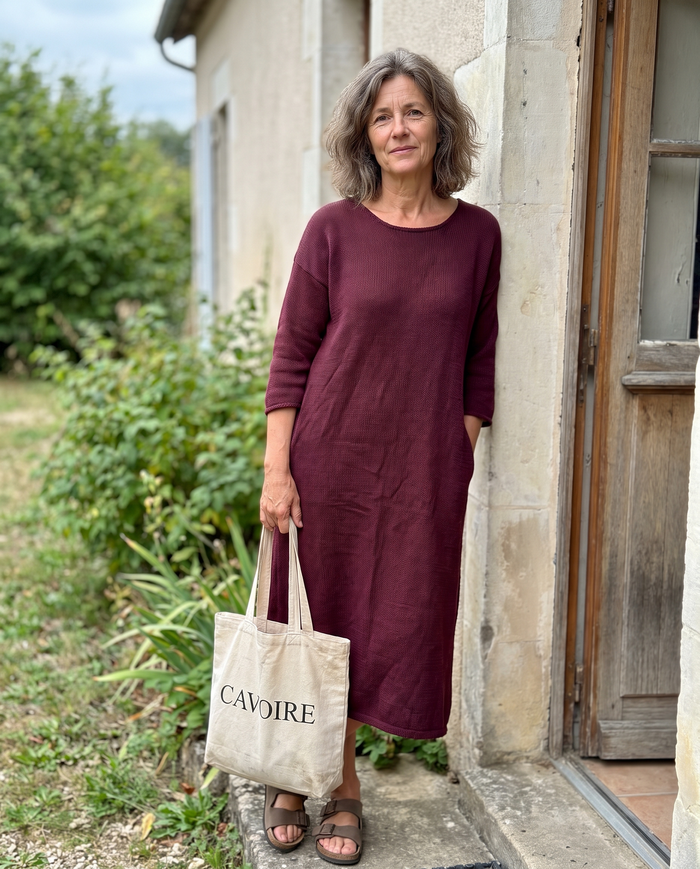 Femme en robe bordeaux dans l'embrasure d'une porte de jardin